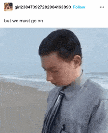 a man in a suit and tie is standing on a beach with a caption that says " but we must go on "