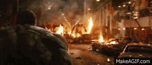 the hulk is standing in the middle of a city street surrounded by burning cars .