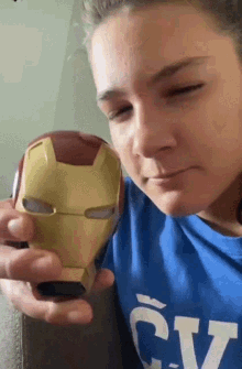 a woman wearing a blue cv shirt is holding a toy iron man mask