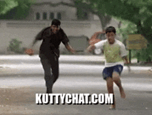 a man and a boy are running down a street with the website kuttychat.com written on the bottom .