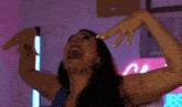 a woman is dancing with her arms outstretched in a room with a neon sign in the background .