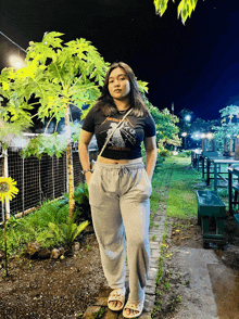 a woman wearing a metallica t-shirt stands in a garden at night