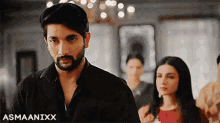 a man with a beard is standing next to a woman in a room with the name asmaanixx on the bottom right