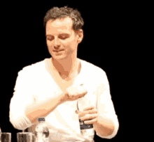 a man in a white shirt sits at a table with a bottle of water and a glass