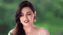 a woman wearing earrings and red lipstick looks at the camera with a green background
