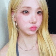 a woman with blonde hair and a barbed wire necklace looks at the camera