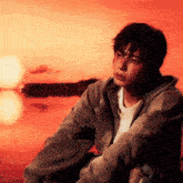 a young man in a hoodie sits in front of a red background