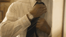 a man is adjusting his tie and wearing a watch .