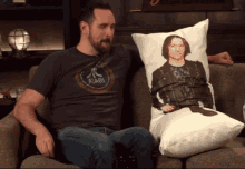 a man wearing an atari shirt sits next to a pillow