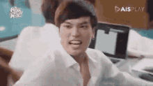 a man in a white shirt is making a funny face while sitting at a desk with a laptop .