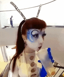 a woman with blue paint on her face holds a blue bottle