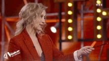 a woman in a red jacket is holding a pencil and the word voice is on her jacket