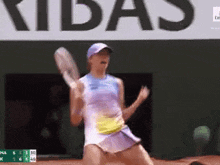 a woman is holding a tennis racquet in front of a sign that says ' ribas '