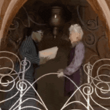 a man and woman are shaking hands in front of a wrought iron railing .