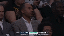 a man in a suit sits in the stands watching a basketball game with espn on the screen