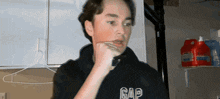 a young man wearing a black gap hoodie holds his hand to his mouth