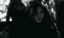 a black and white photo of a woman in a hooded jacket standing in a crowded street .