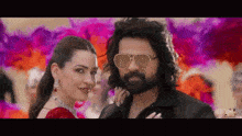 a man and a woman are posing for a picture . the man is wearing sunglasses and the woman is wearing earrings .