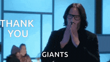 a man with glasses is clapping his hands in front of a thank you giants sign