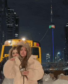 two girls stand in front of a yellow school bus