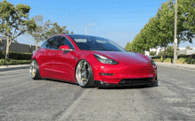 a red tesla model 3 is parked on the side of the road .