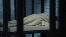 a person laying in a jail cell with a blanket on