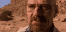 a man with glasses and a beard is looking at the camera .