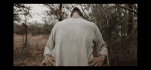 a man in a gray shirt is standing in a field with his hands on his hips