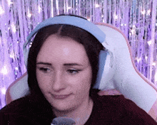 a woman wearing headphones is sitting in front of a purple curtain .