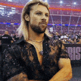 a man with long blonde hair and a beard is standing in front of a crowd wearing a black shirt and a necklace .