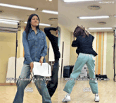 a woman in a denim shirt is holding a piece of paper and dancing with a man in a black jacket behind her