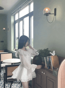 a woman in a white dress is standing in front of a bookshelf with a book titled be tough