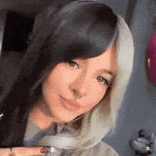 a woman with black and white hair and a nose ring is looking at the camera .