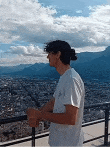 a man in a white shirt is standing on a balcony overlooking a city