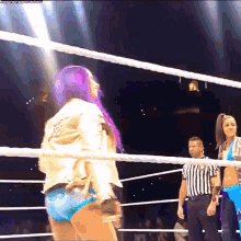 a female wrestler with purple hair is standing in a wrestling ring .
