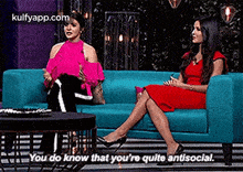 two women are sitting on a blue couch and talking .