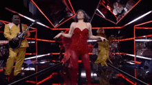 a woman in a red dress is dancing on a stage with a band behind her .