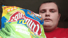 a man in a red shirt is holding a bag of chips