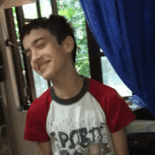 a young man wearing a red and white sports shirt smiles with his eyes closed
