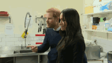 a man and a woman are standing in a kitchen with a sign on the wall that says ' bread ' on it