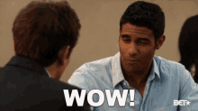 a man in a blue shirt is talking to another man and says wow