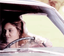 a woman is sitting in a car holding the steering wheel .