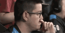 a man wearing glasses and headphones is sitting in a stadium and holding his nose .