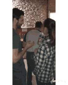 a woman in a plaid shirt is holding a bottle of water while standing next to a man in a black shirt .