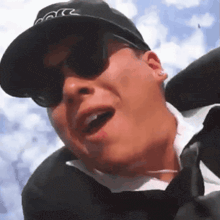 a man wearing a hat and sunglasses is making a funny face with his mouth open