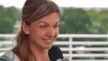 a woman is talking into a microphone and smiling while standing in front of a fence .