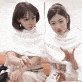 two women sitting next to each other wearing white shawls on their heads