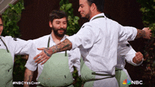 a group of men hugging each other with a nbc logo in the background
