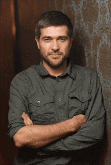 a man with his arms crossed wears a black sweatshirt with a cross on the front