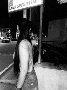 a black and white photo of a woman standing under a sign that says max speed limit